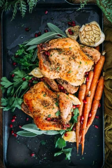 Roasted hens with pomegranate and carrots on a black plate.