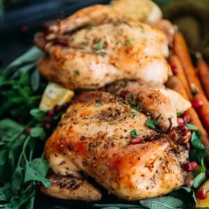 Roasted Cornish hens with pomegranate and herbs on a black plate.
