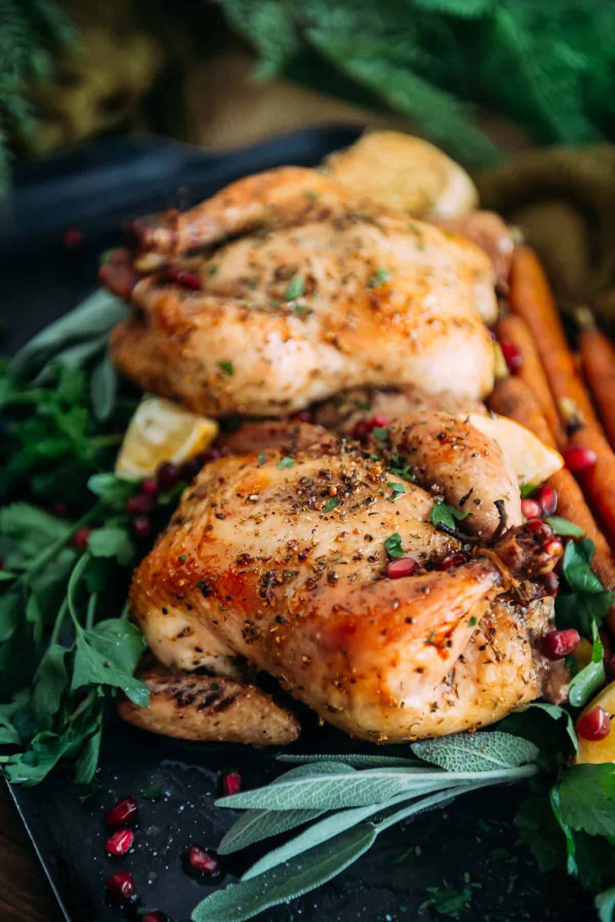 Roasted Cornish hens with pomegranate and herbs on a black plate.