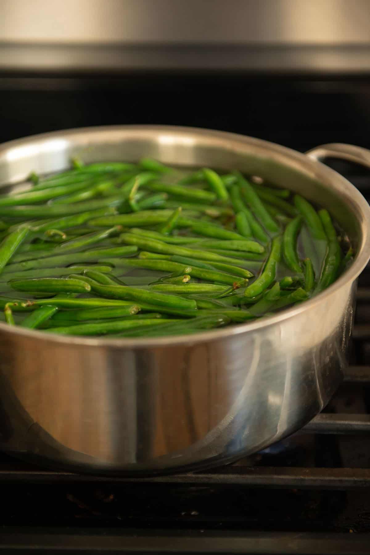 A pan filled with green beans on a stove top.
