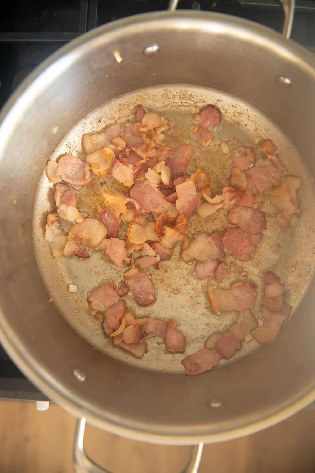 A pan on a stove with bacon in it.