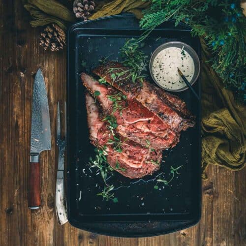 Sliced reverse seared prime rib on a baking sheet with herbs and spices.