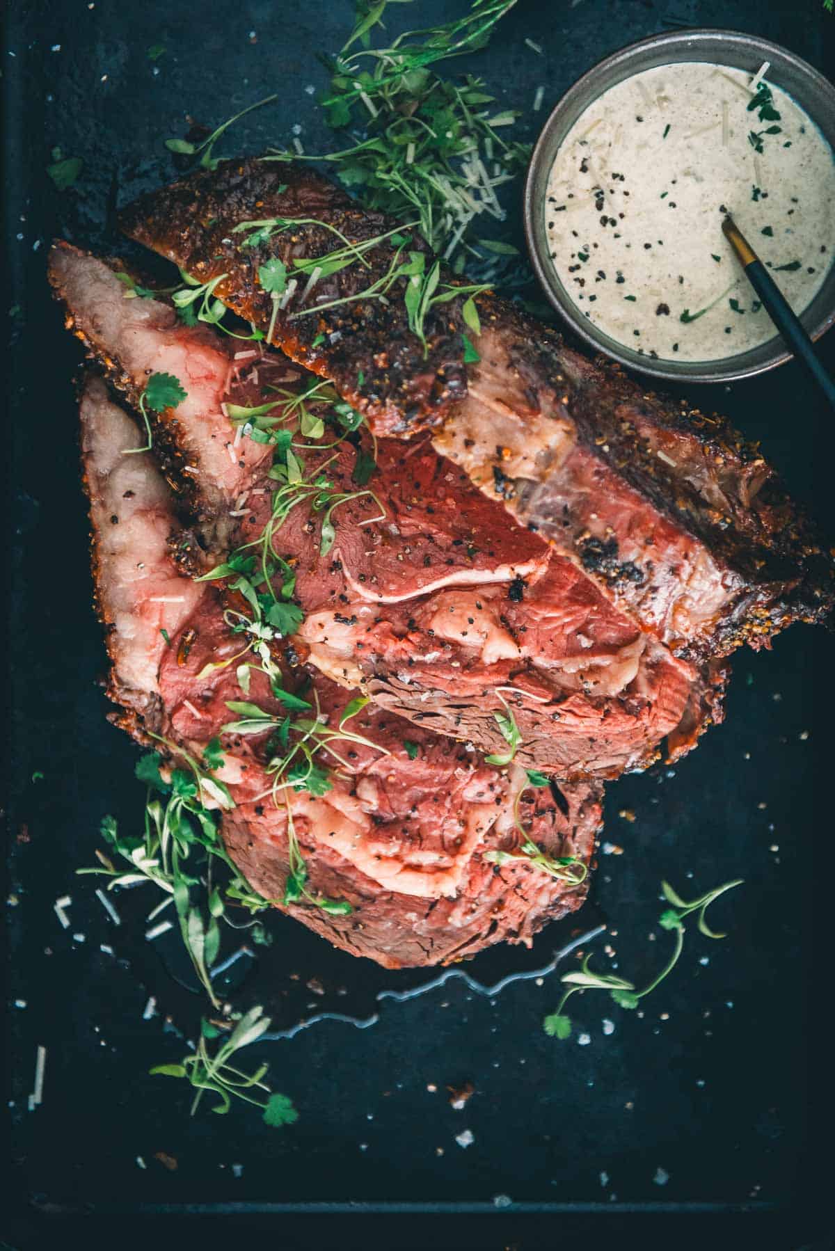 A sliced reverse seared prime rib on a tray with a horseradish sauce on it.