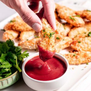 A person dipping chicken tenders in a sauce.