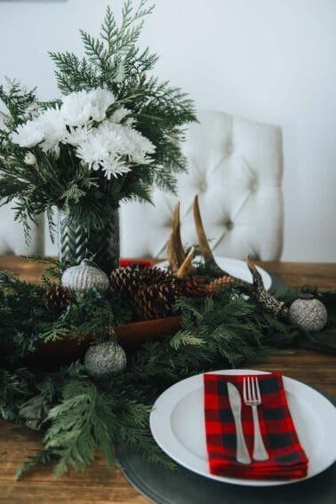 A christmas table setting with pine cones and buffalo check napkin.