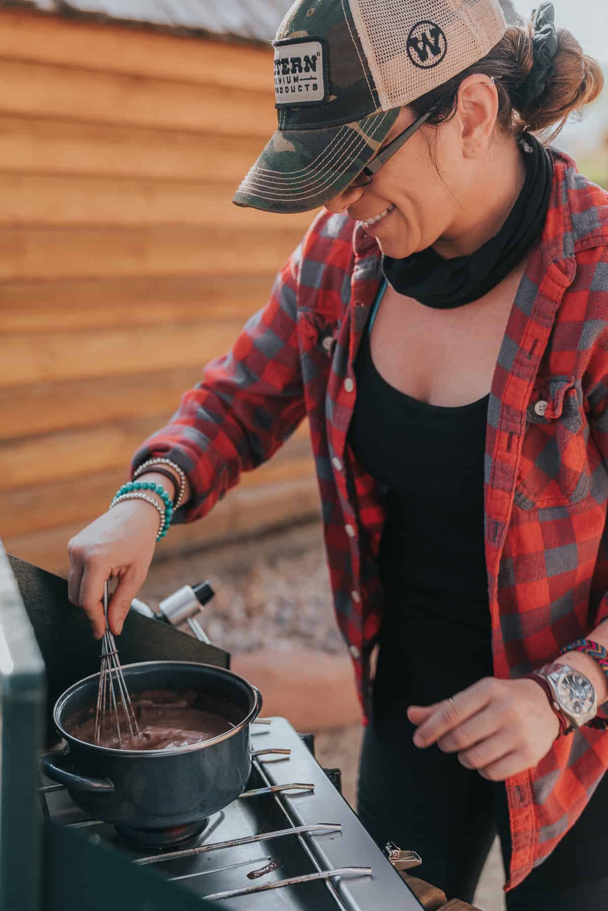 A woman wearing a hat and a plaid shirt cooking on a grill.