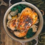 Roasted chicken in a Dutch oven on a wooden table ready to be served.