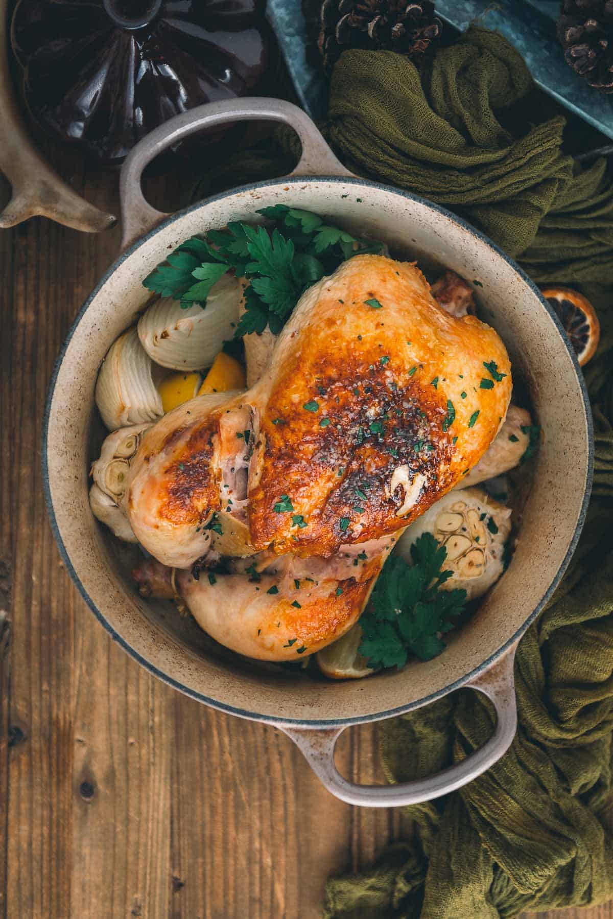 Roasted chicken in a Dutch oven on a wooden table ready to be served.
