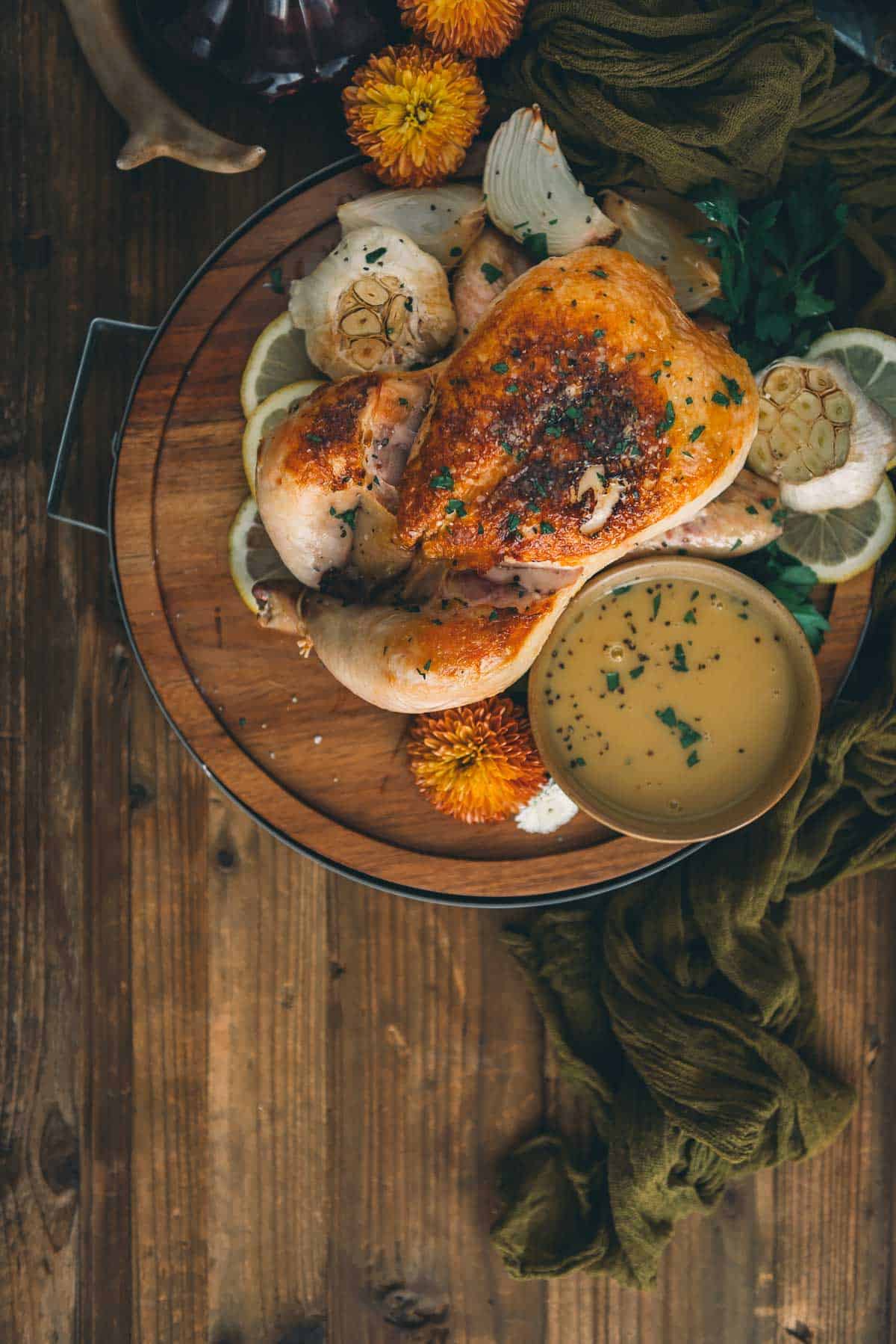 Roasted chicken with white wine pan sauce on a wooden table.