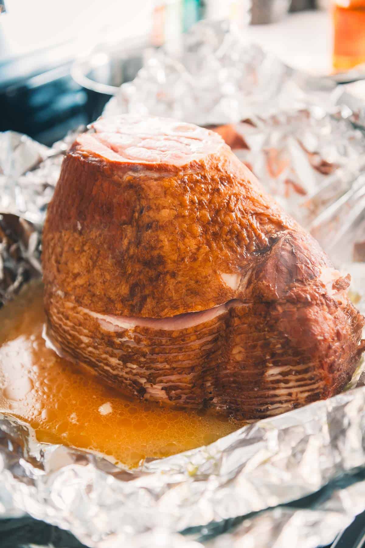 A ham wrapped in foil sitting on top of a stove in ham juices.