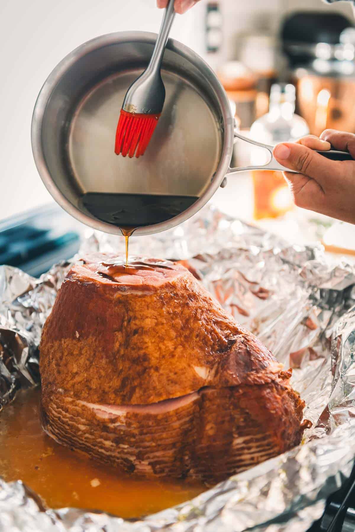 A person pouring a glaze over a roasted ham.
