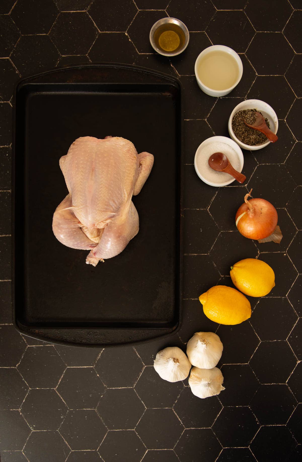 A chicken on a cutting board with lemons and other ingredients for this recipe.