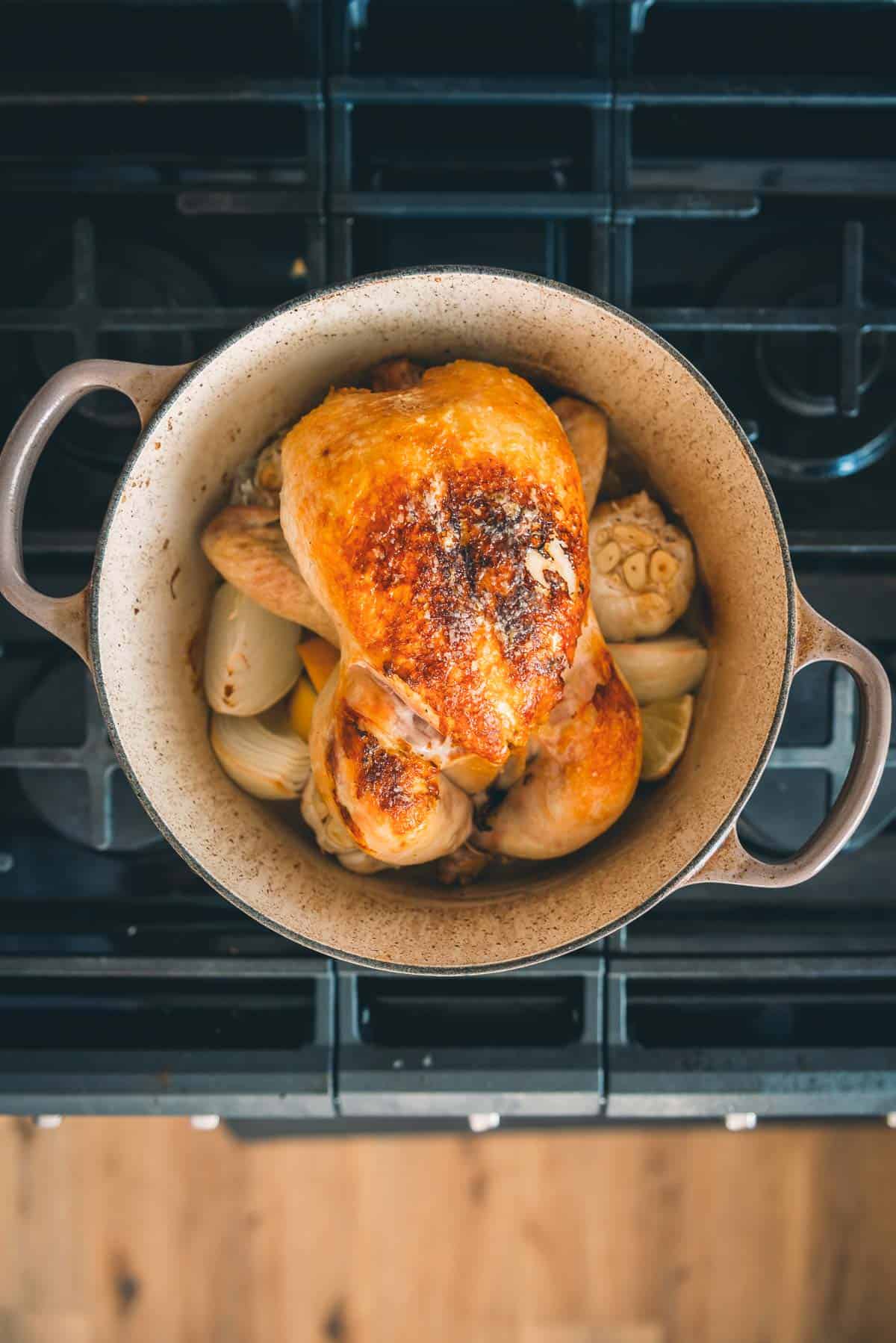 Golden brown chicken in a pan on a stove top after being roasted.