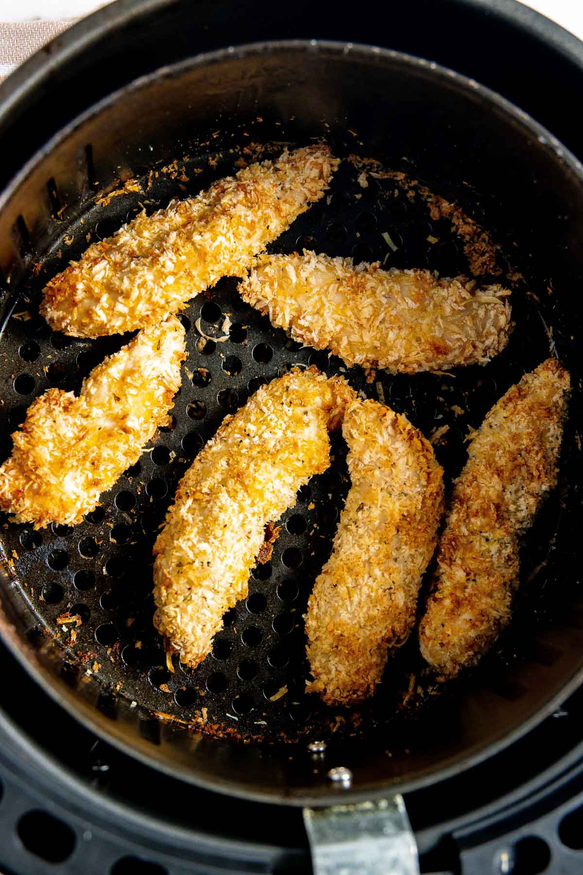 Chicken strips in an air fryer basket.