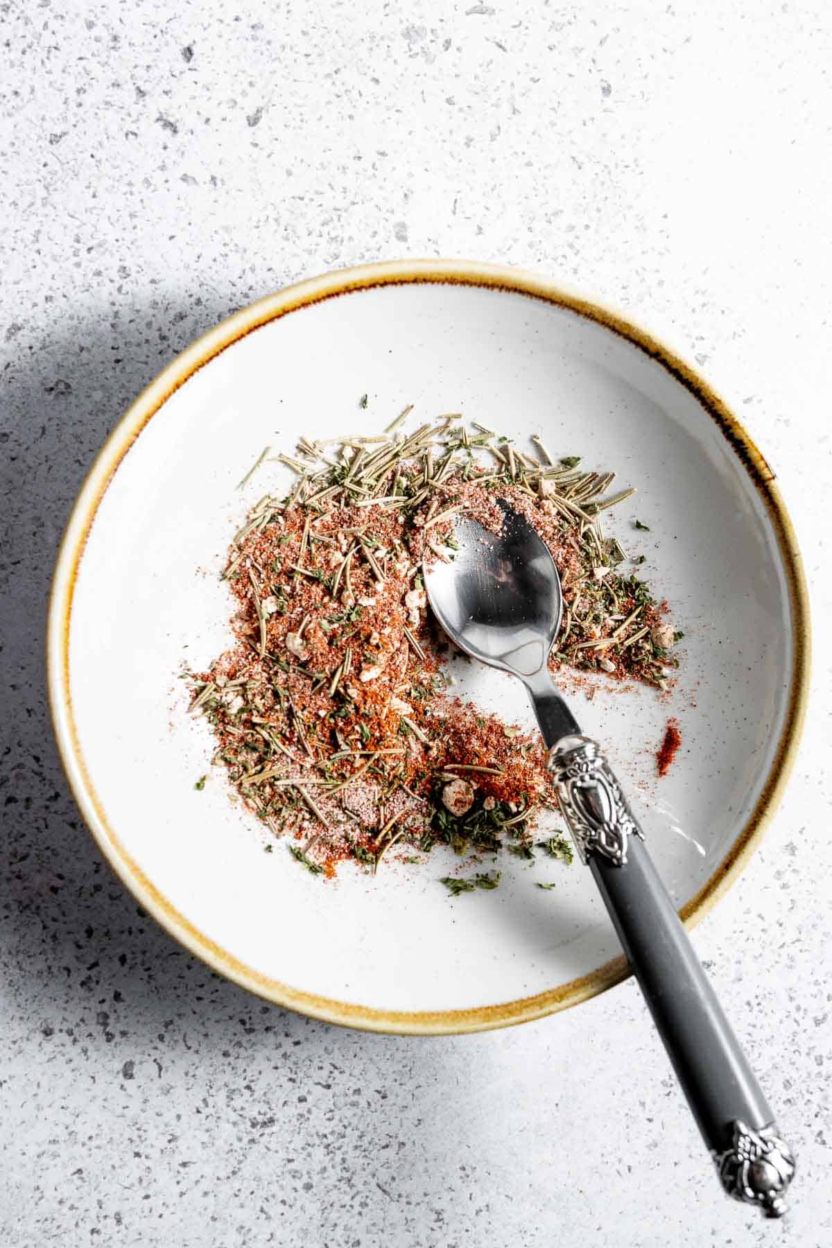A white bowl with a spoon and herbs in it.