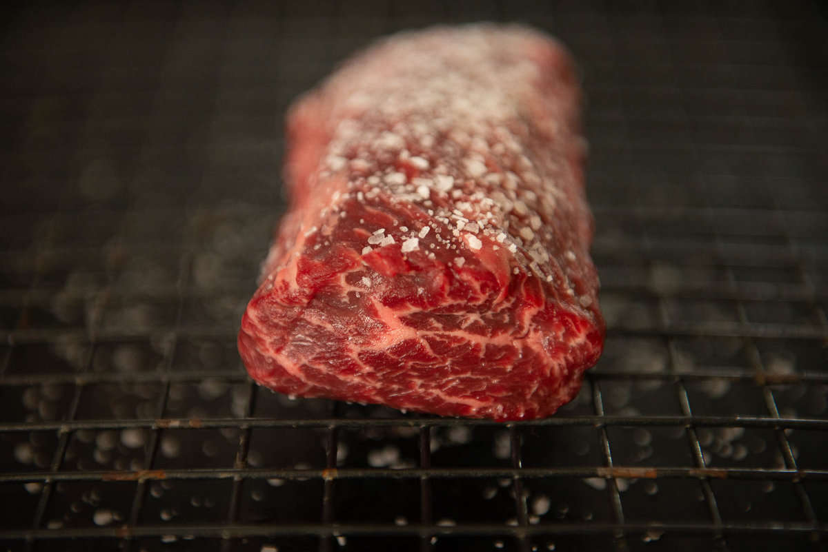 A piece of steak sitting on a rack showing marbling from the side.