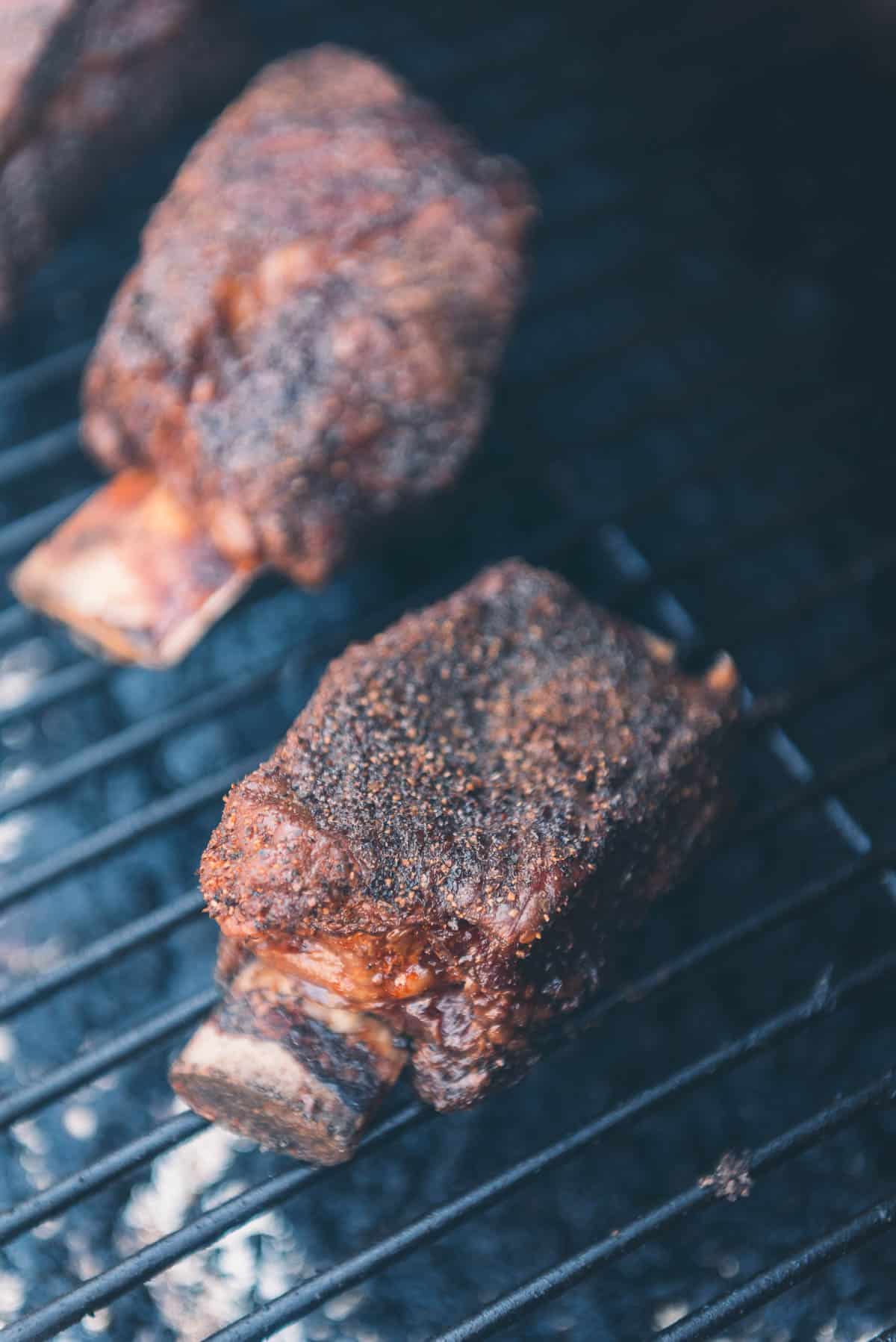 Short ribs being smoked on a grill.