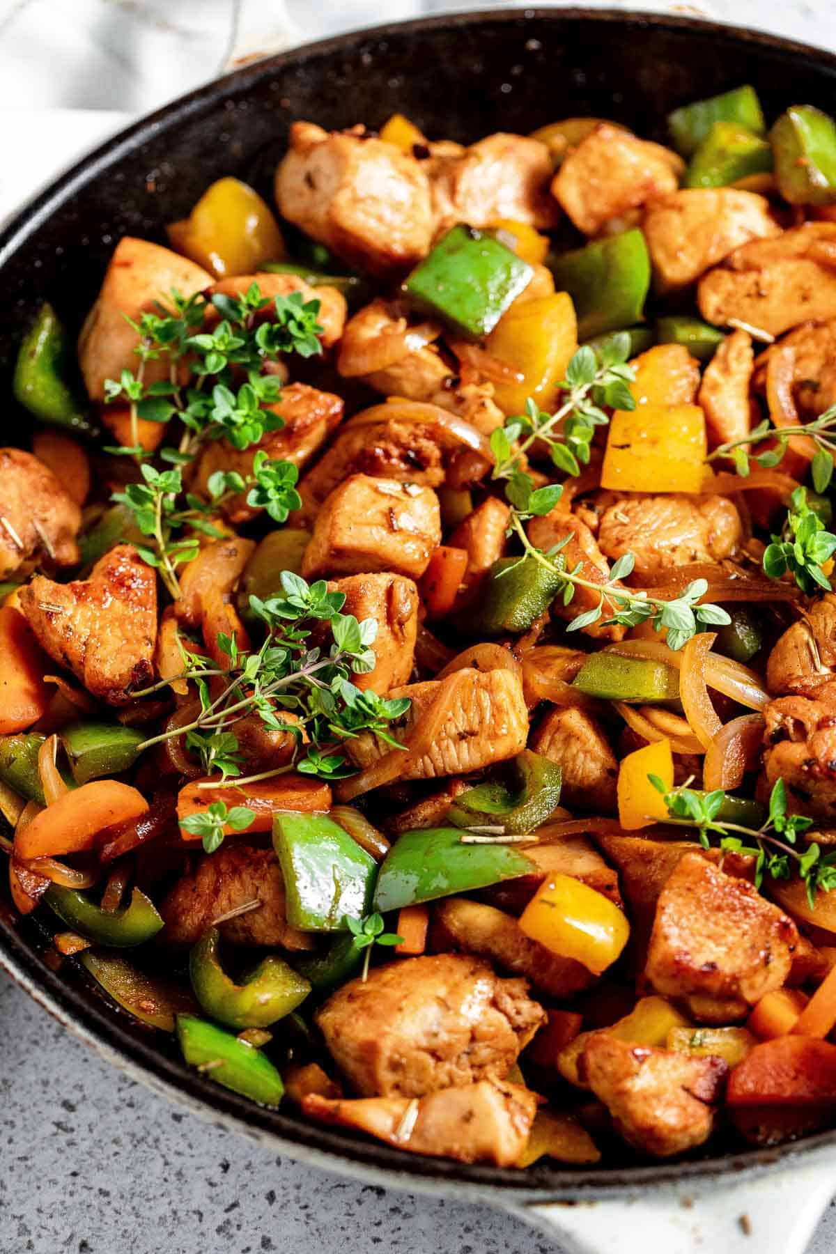 Chicken stir fry in a skillet with peppers and herbs.
