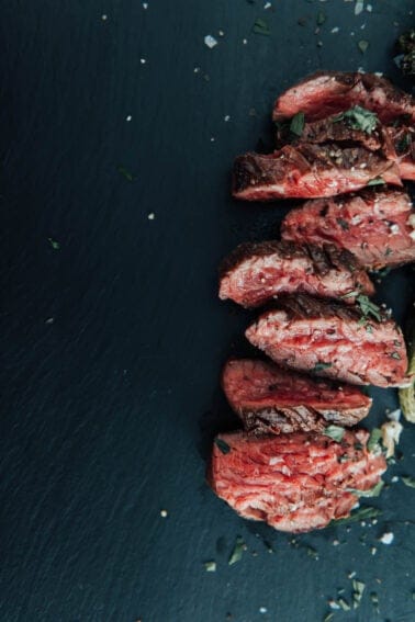 Slices of hanger steak on a black table.