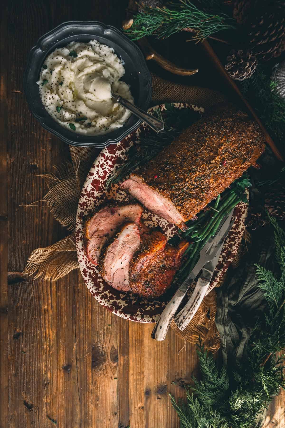 A platter of smoked rack of pork and mashed potatoes on a wooden table.
