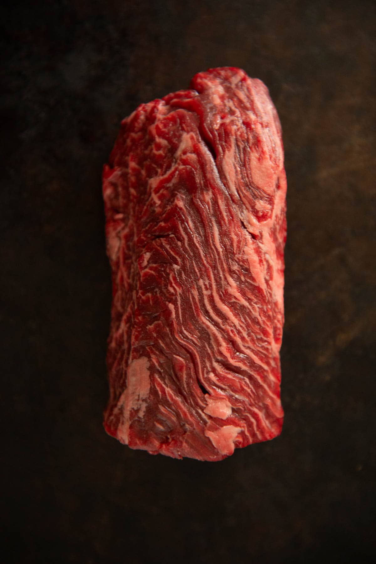 A close up of a piece of wagyu hanger steak on a dark surface.