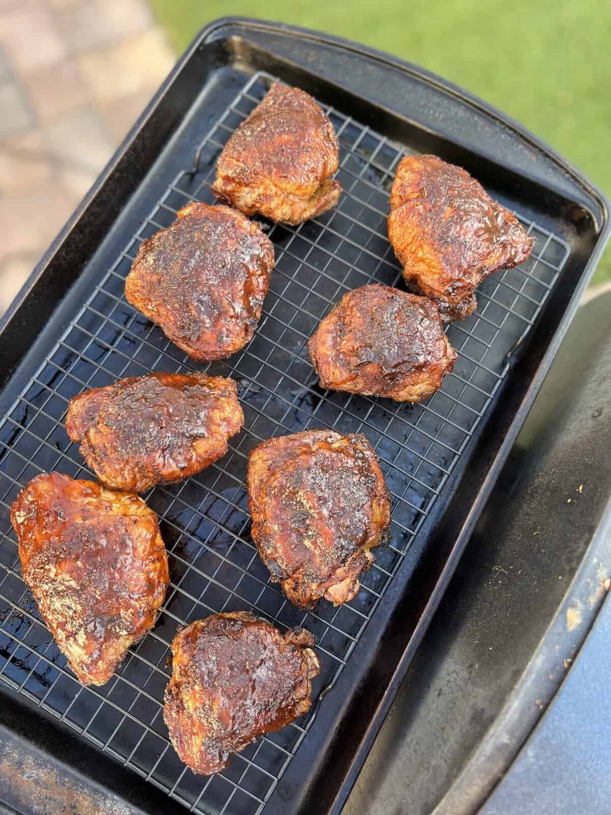 Smoked chicken thighs on a baking sheet on the side of a grill.