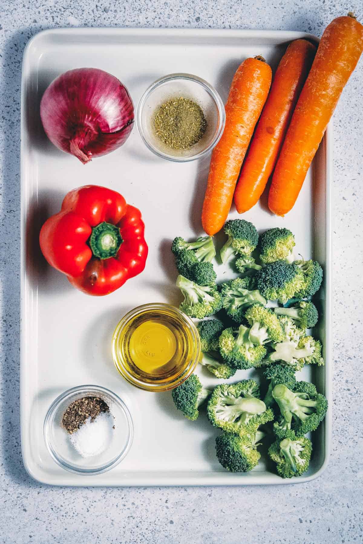 A tray with broccoli, carrots, onions and spices.