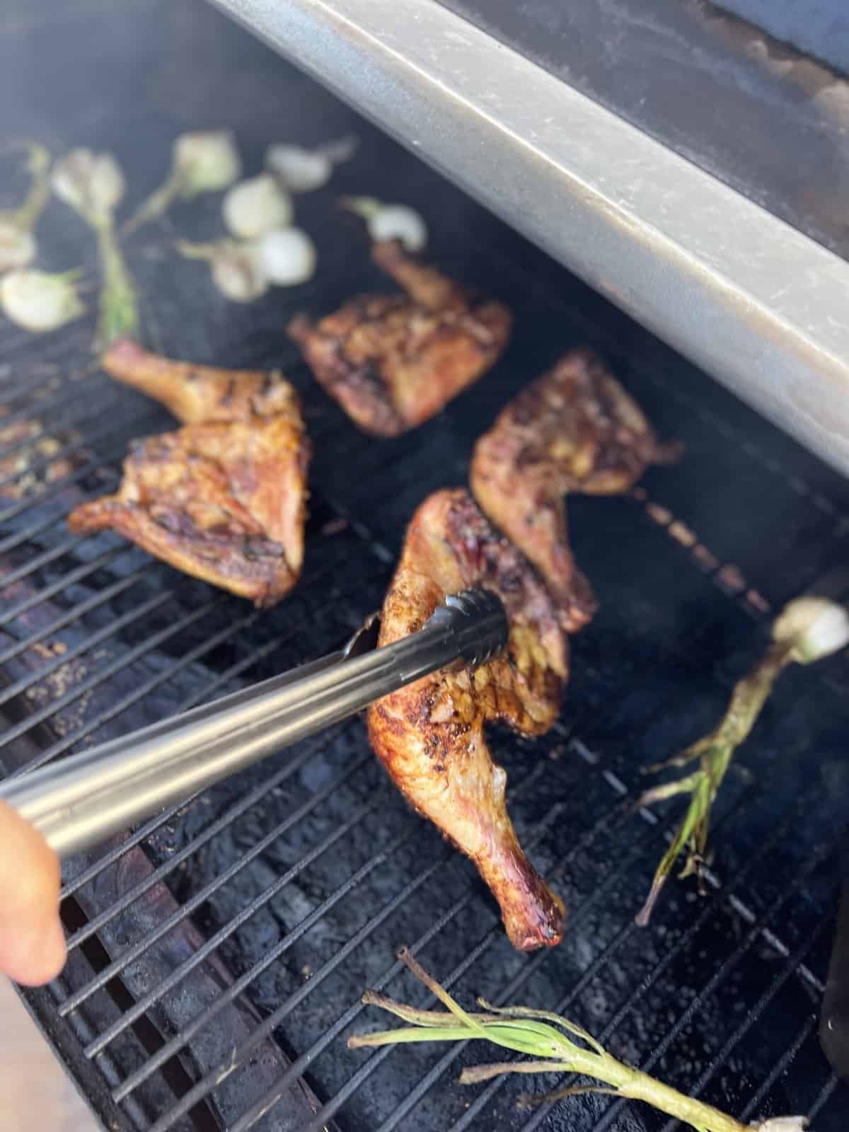 A person is using a spatula to cook chicken legs on a grill.