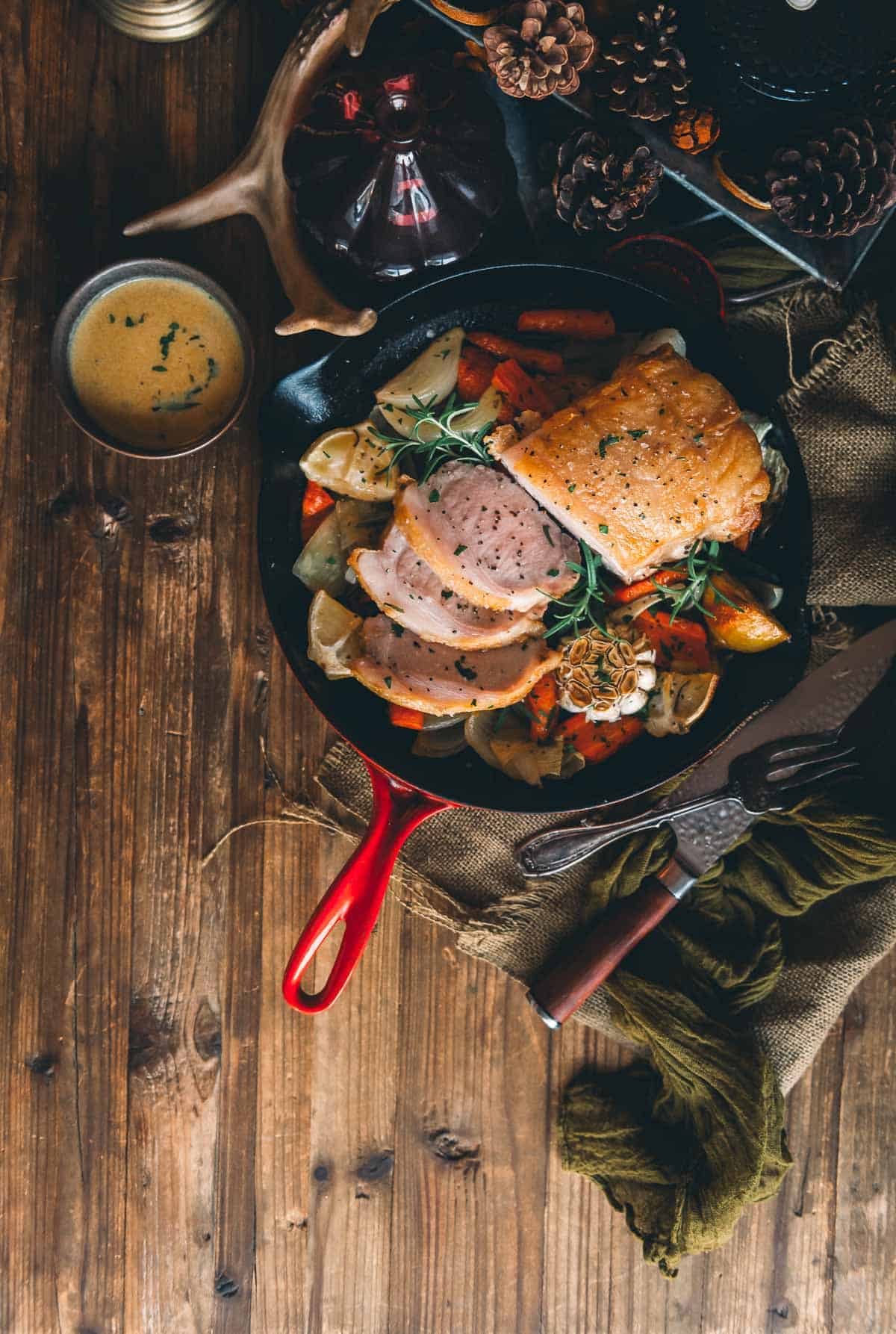 A cast iron skillet with roasted pork loin and vegetables on a wooden table.