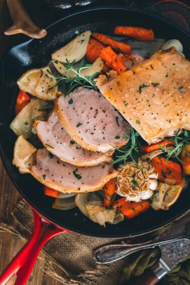 Pork loin and vegetables in a skillet on a wooden table.