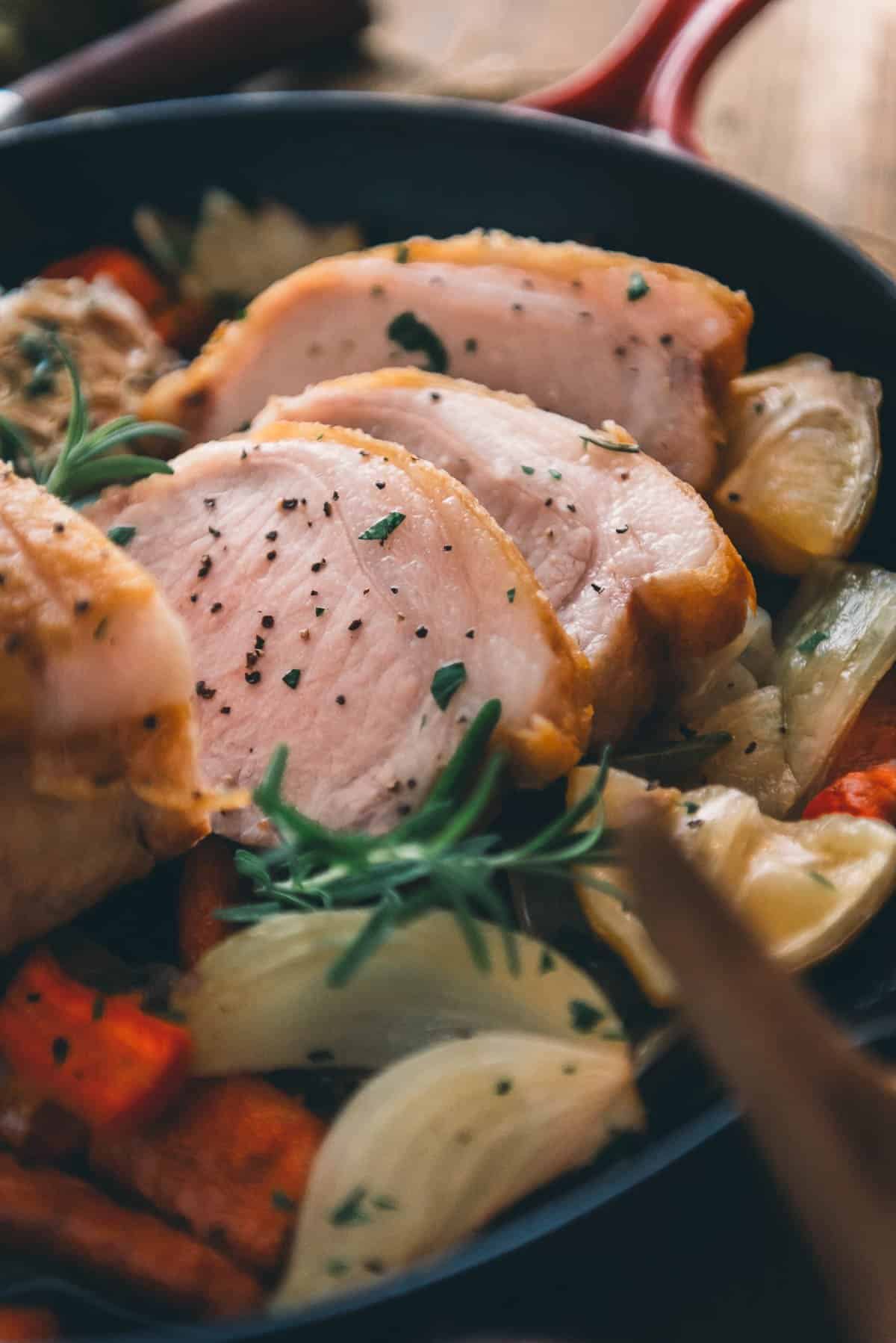 A cast iron skillet full of pork slices and vegetables on a table.