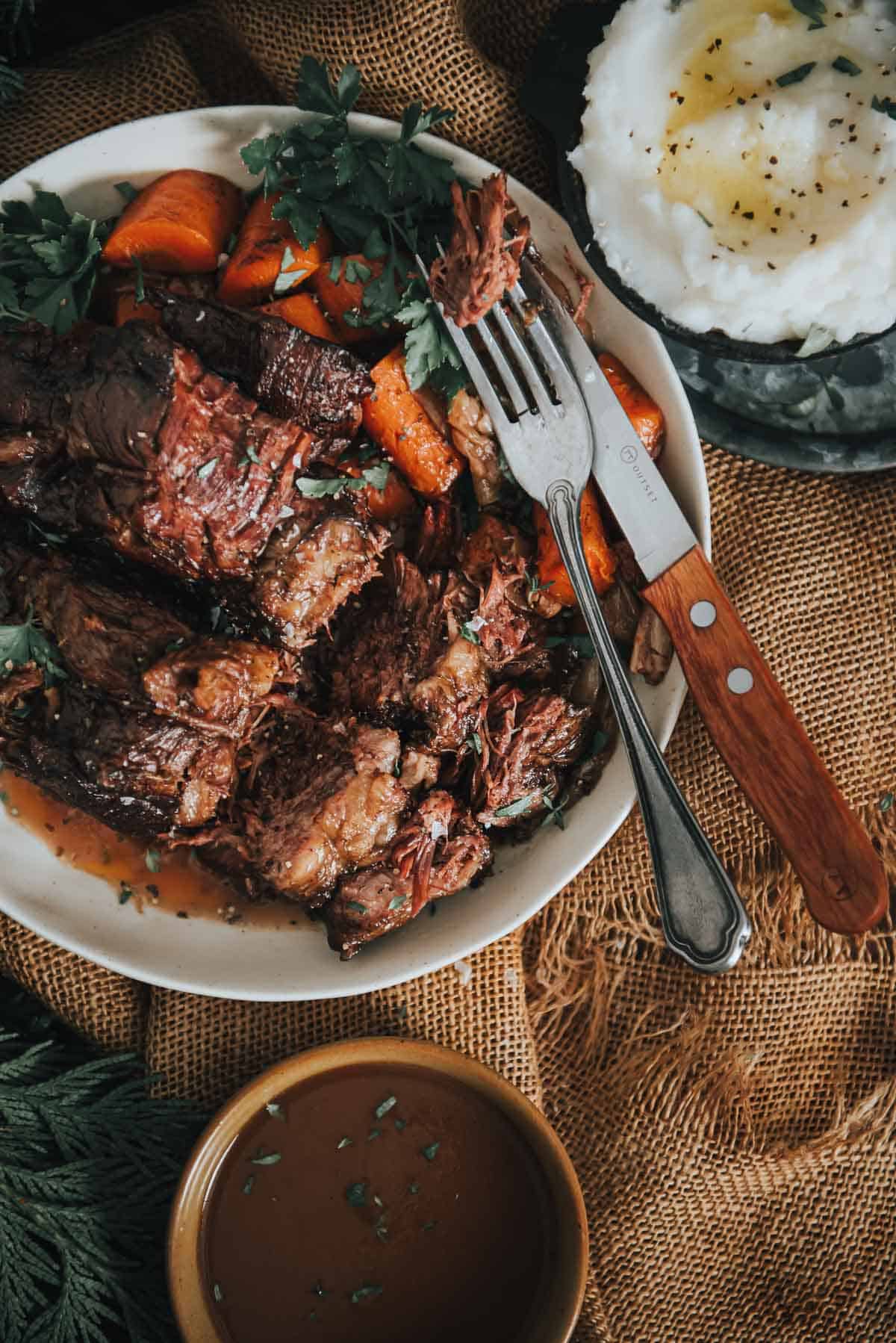 Slow cooker pot roast on a platter with carrots and gravy.