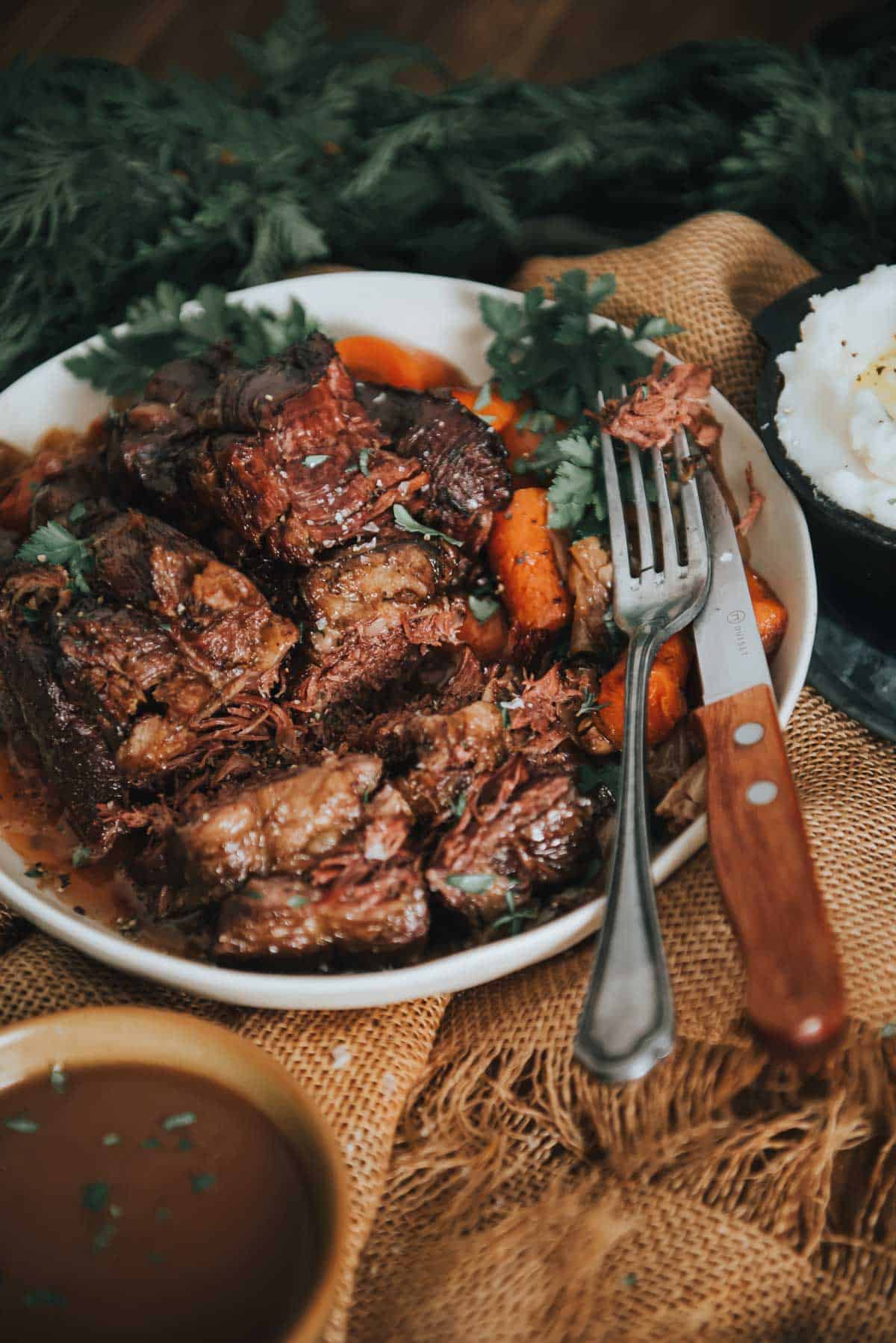 A slow cooker pot roast on a white plate with gravy and carrots.