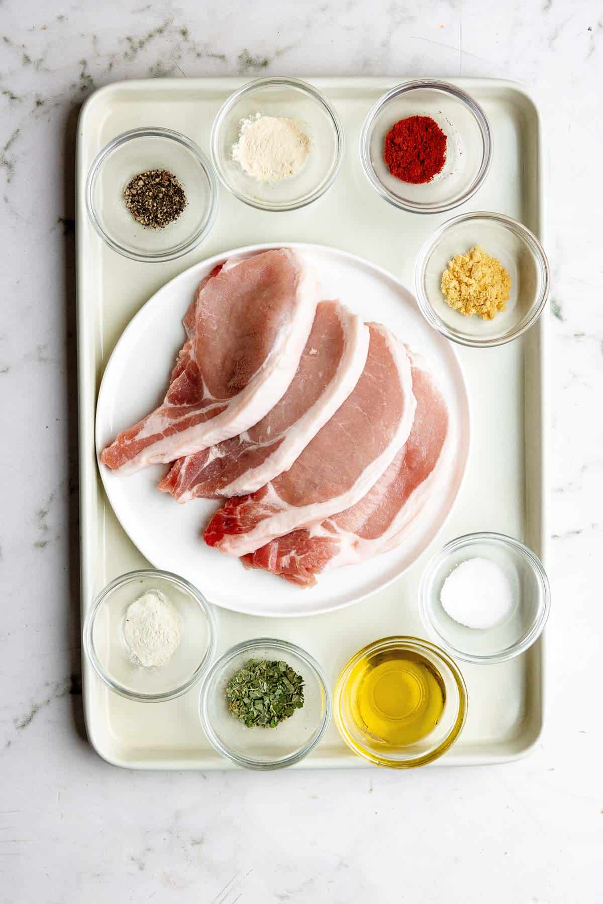 A tray with pork chops and seasonings on it.