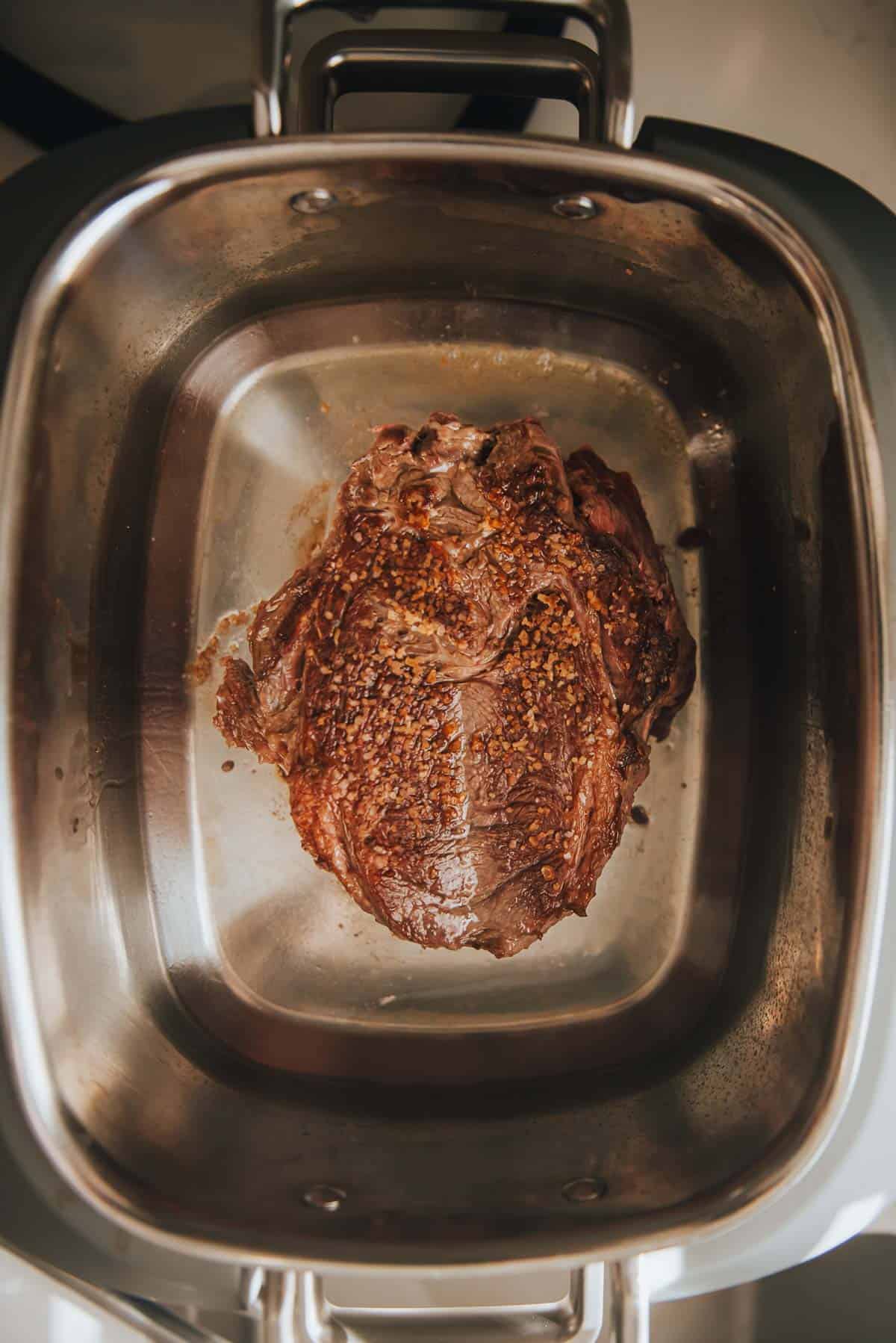 A chuck roast being browned in a slow cooker.