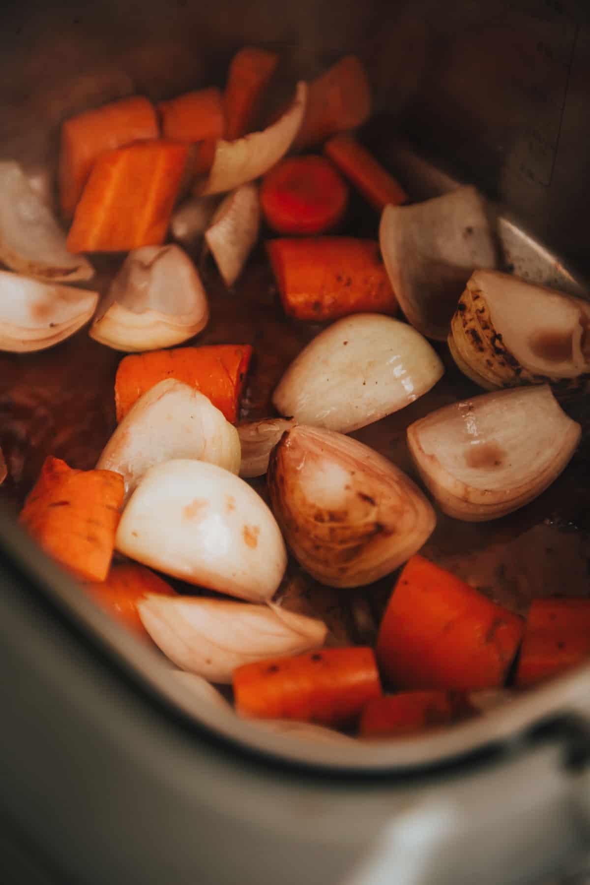 Carrots and onions are being cooked in a slow cooker.