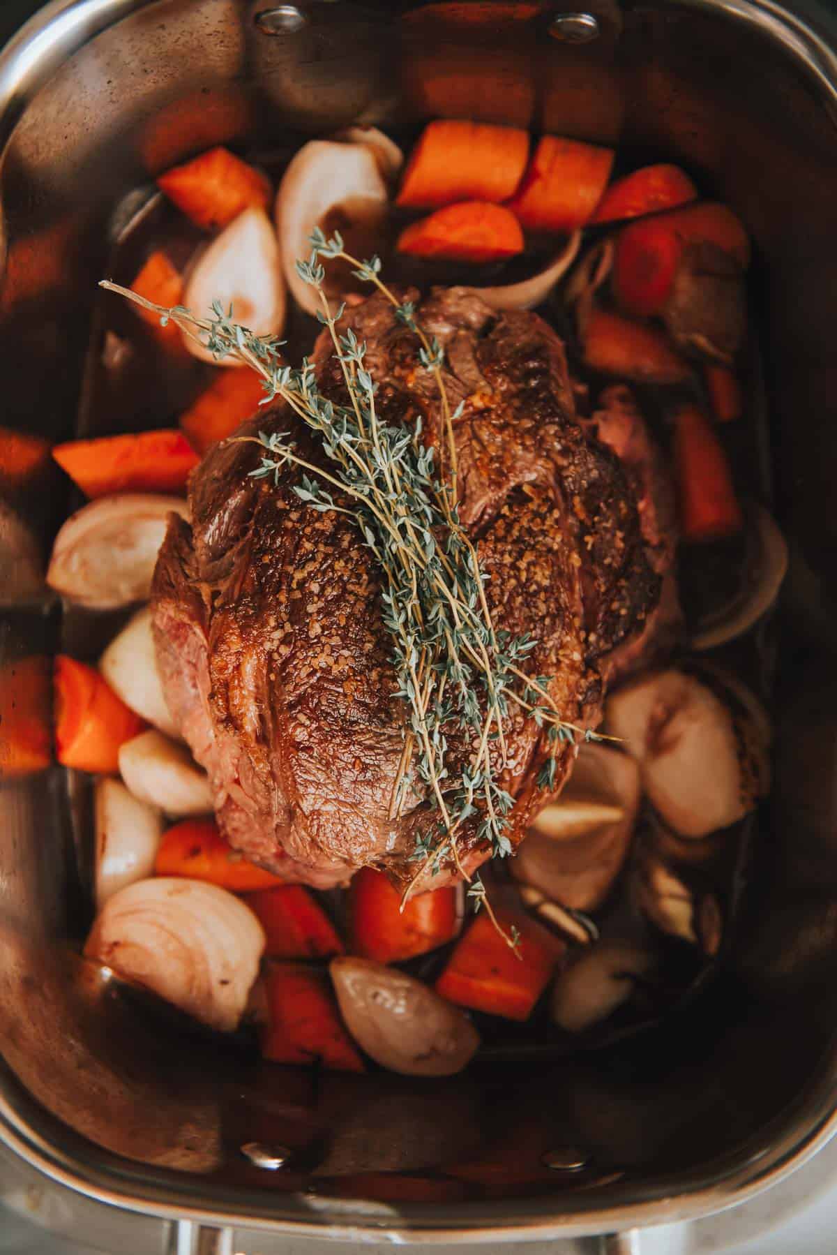 Slow cooker chuck roast with carrots and sprigs of thyme.