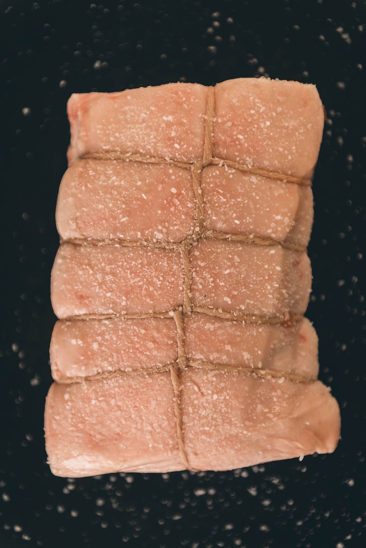 A close up of a piece of pork thats been salted on a black surface.