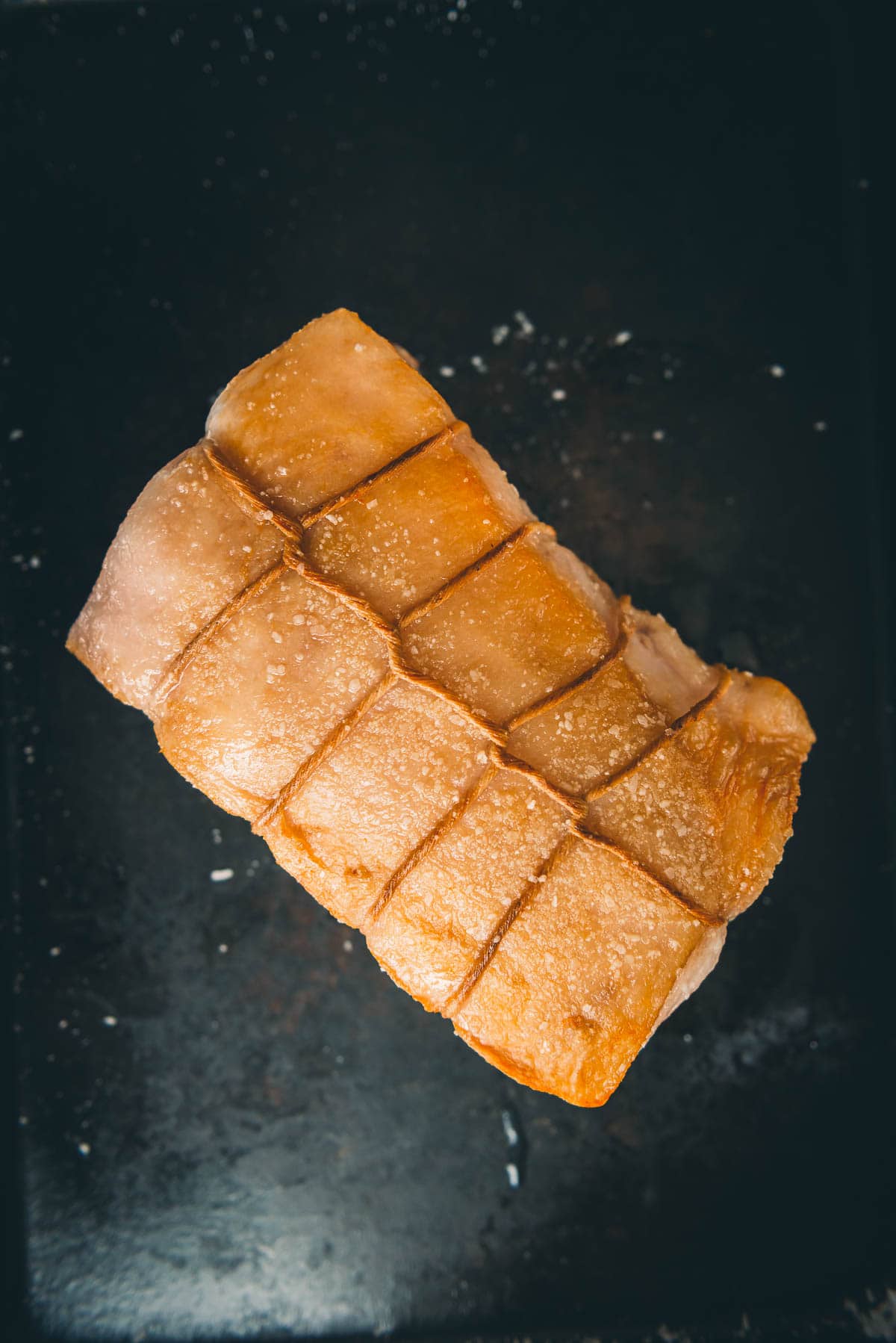 A pork loin on a baking sheet to show the crispy skin.