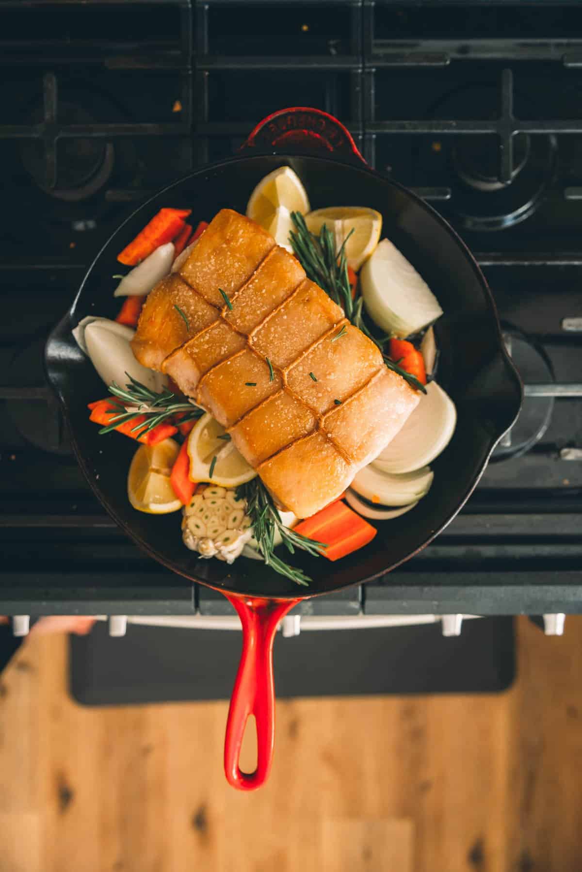 A skillet filled vegetables and a pork loin on a stove top.