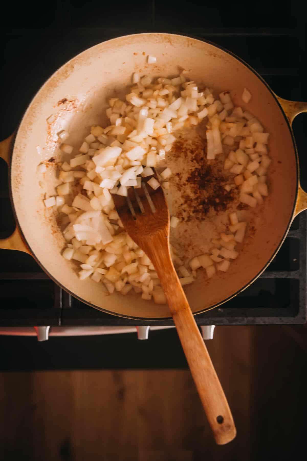 A braising pan with onions and a wooden spoon.