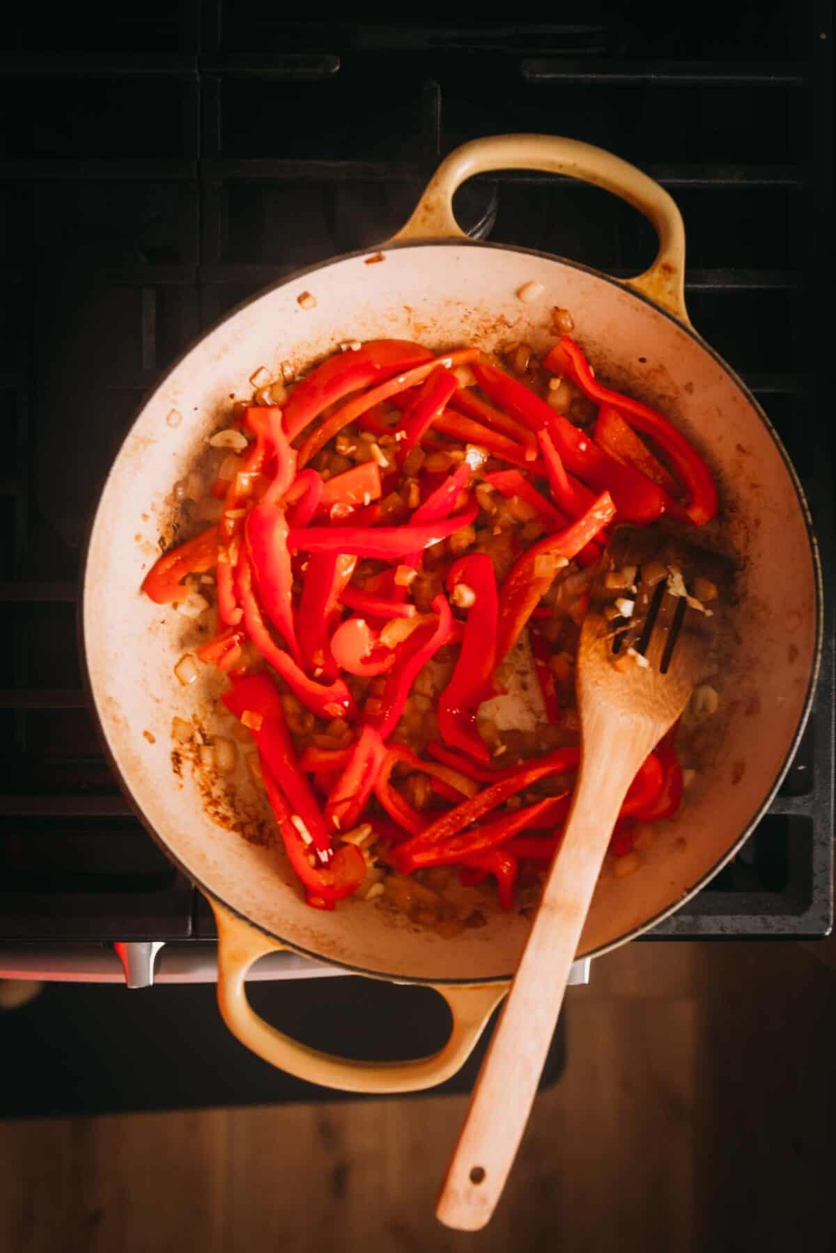 A braising pot with peppers and a wooden spoon.
