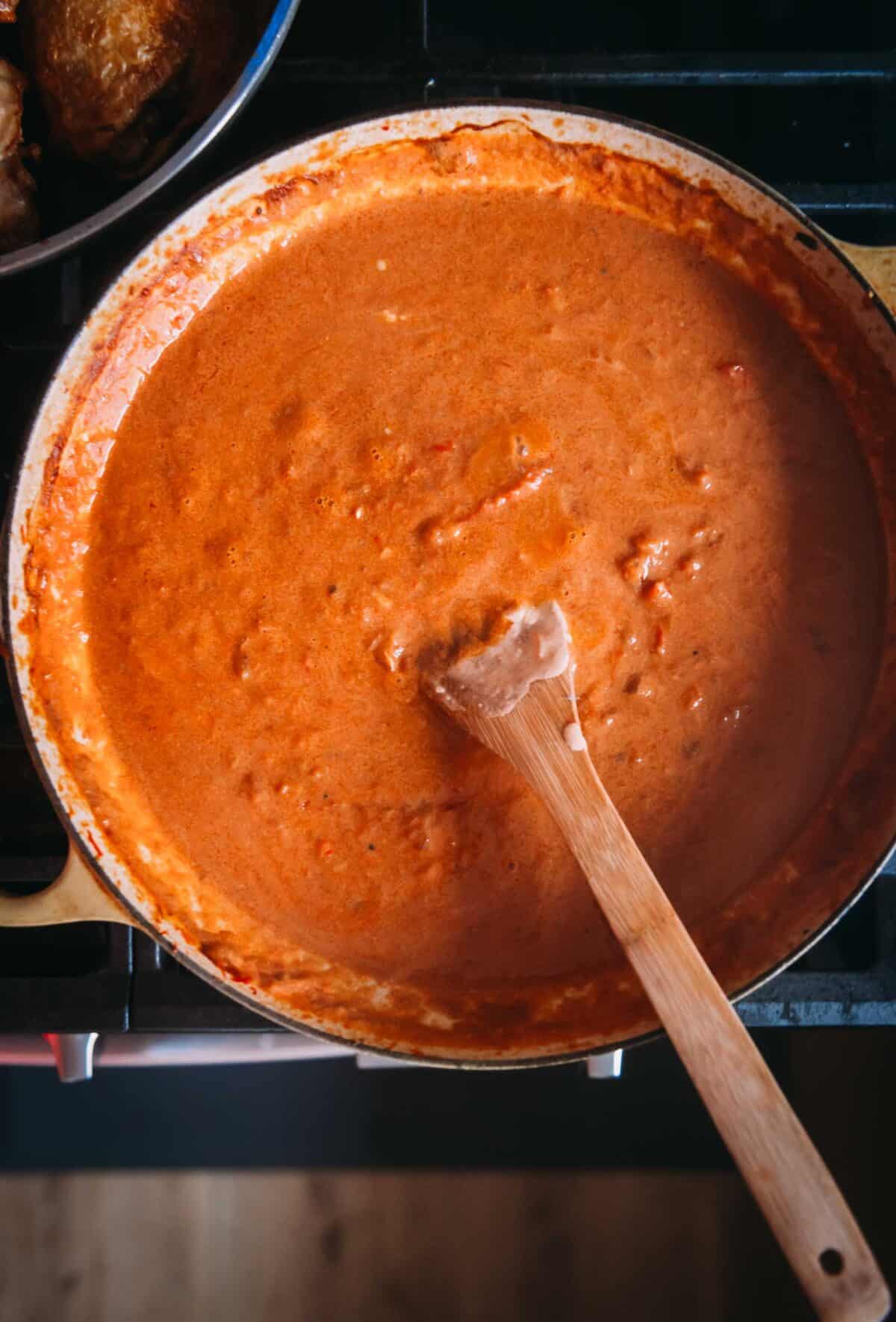 A pot of paprika sauce on a stove with a wooden spoon.