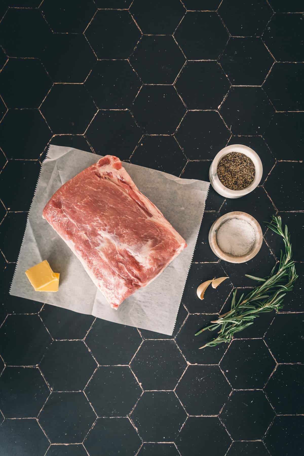 A pork loin on a cutting board with herbs and spices.