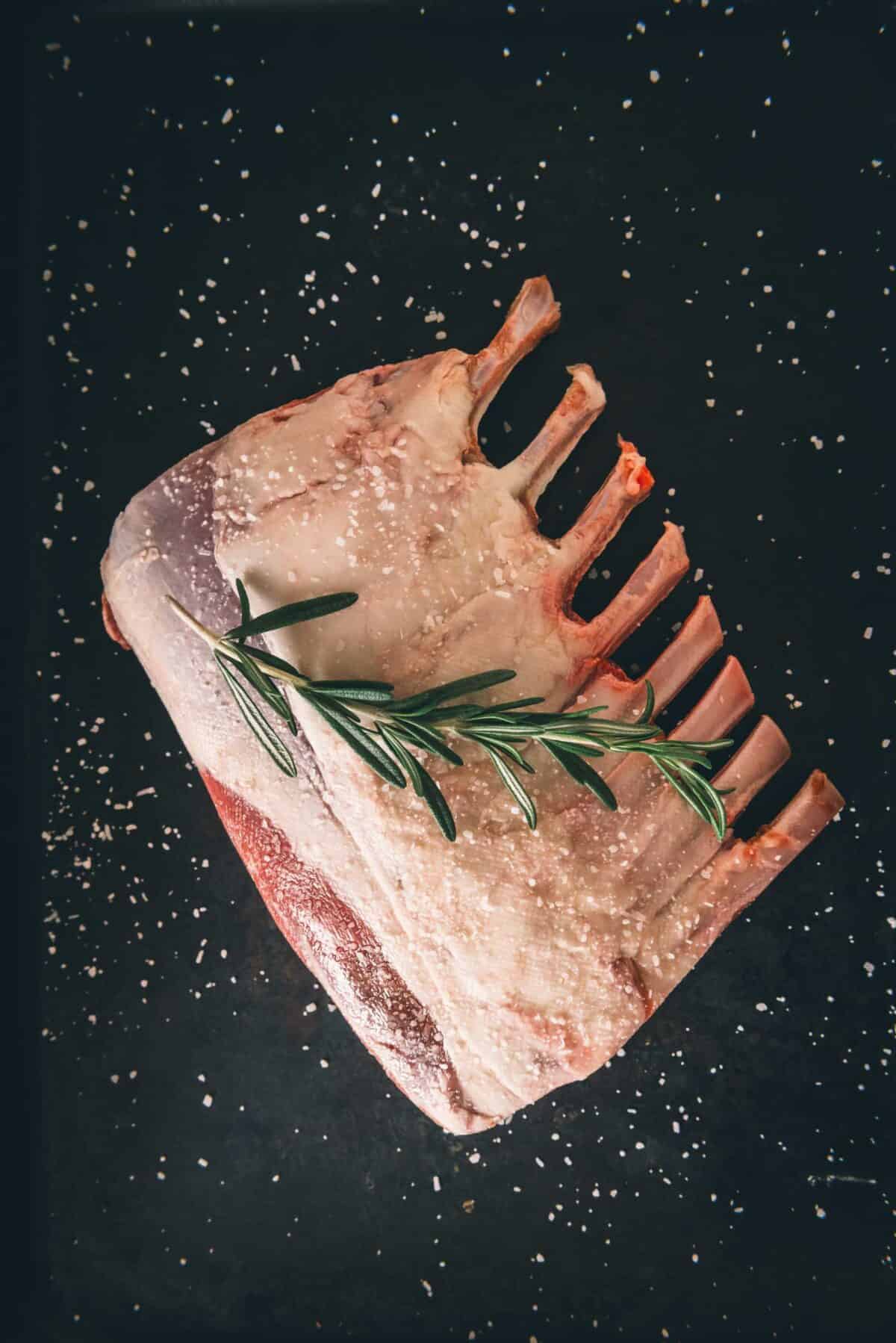 A piece of lamb with a rosemary sprig on a black background.