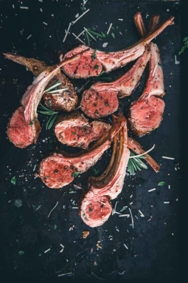 Sous vide rack of lamb sliced into chops on a black tray with rosemary sprigs.
