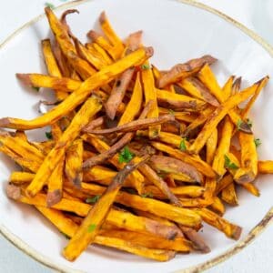 Sweet potato fries in a white bowl with parsley.