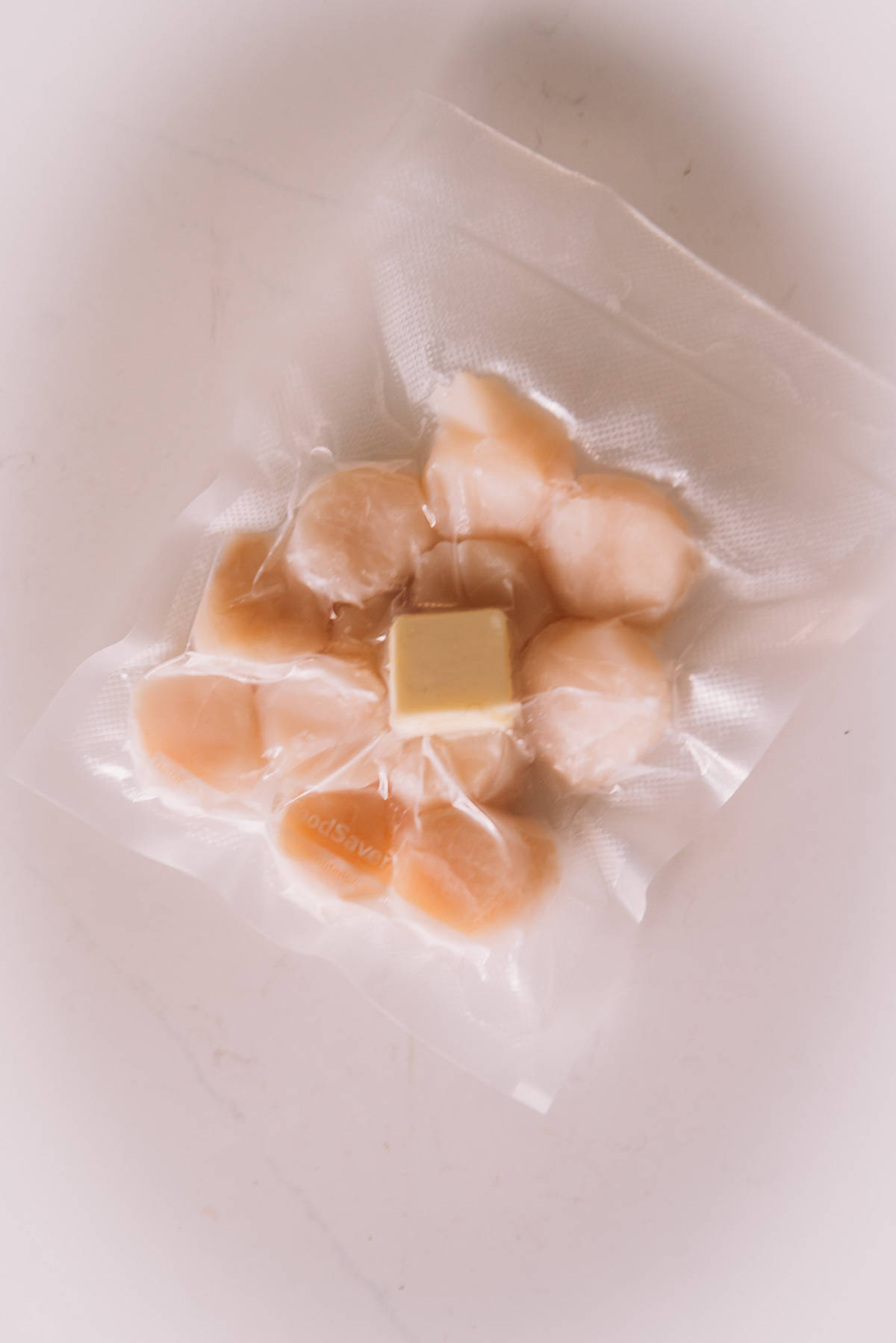 A vacuum sealed bag of sea scallops with a piece of butter in it.