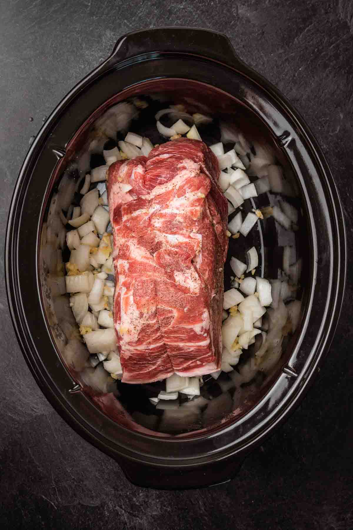 A piece of meat in a slow cooker with onions.