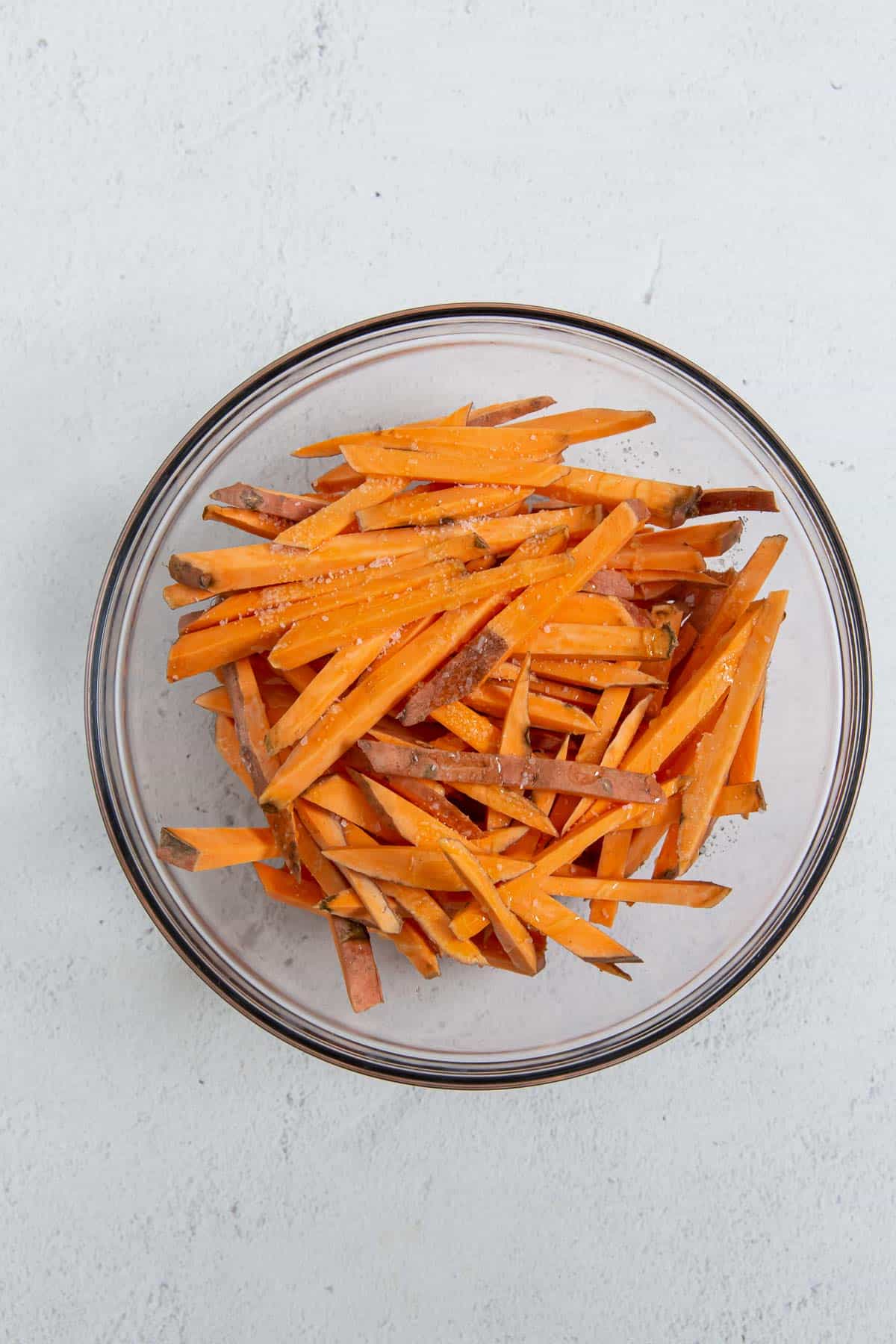 Sweet potato fries in a glass bowl on a gray background.